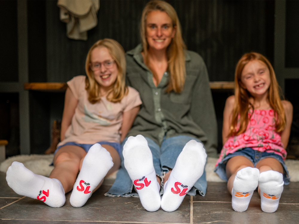 Two women and two girls wearing socks with a logo, sitting on a bench.